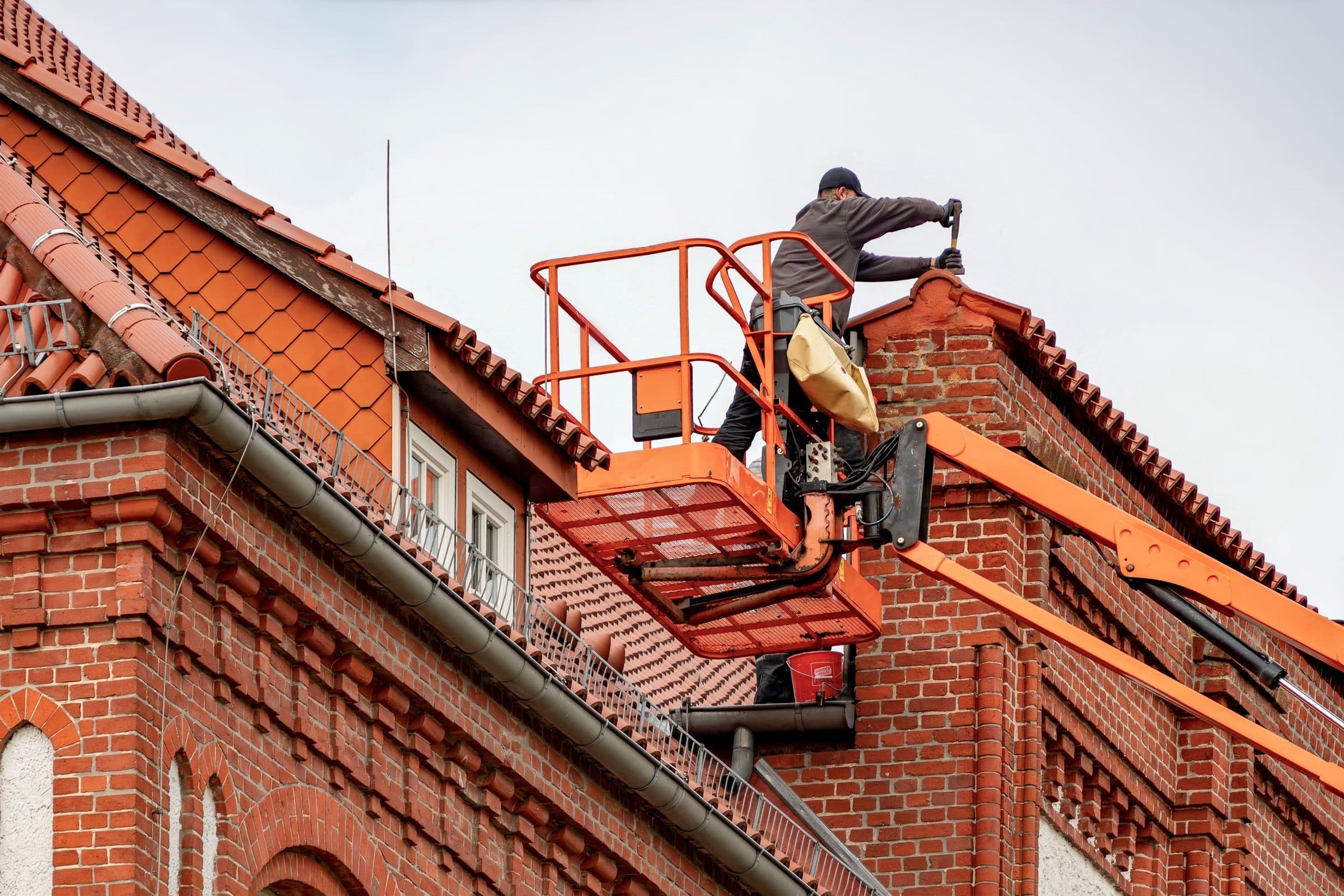 A roofer on a cherry picker working along the roofline of a red brick building