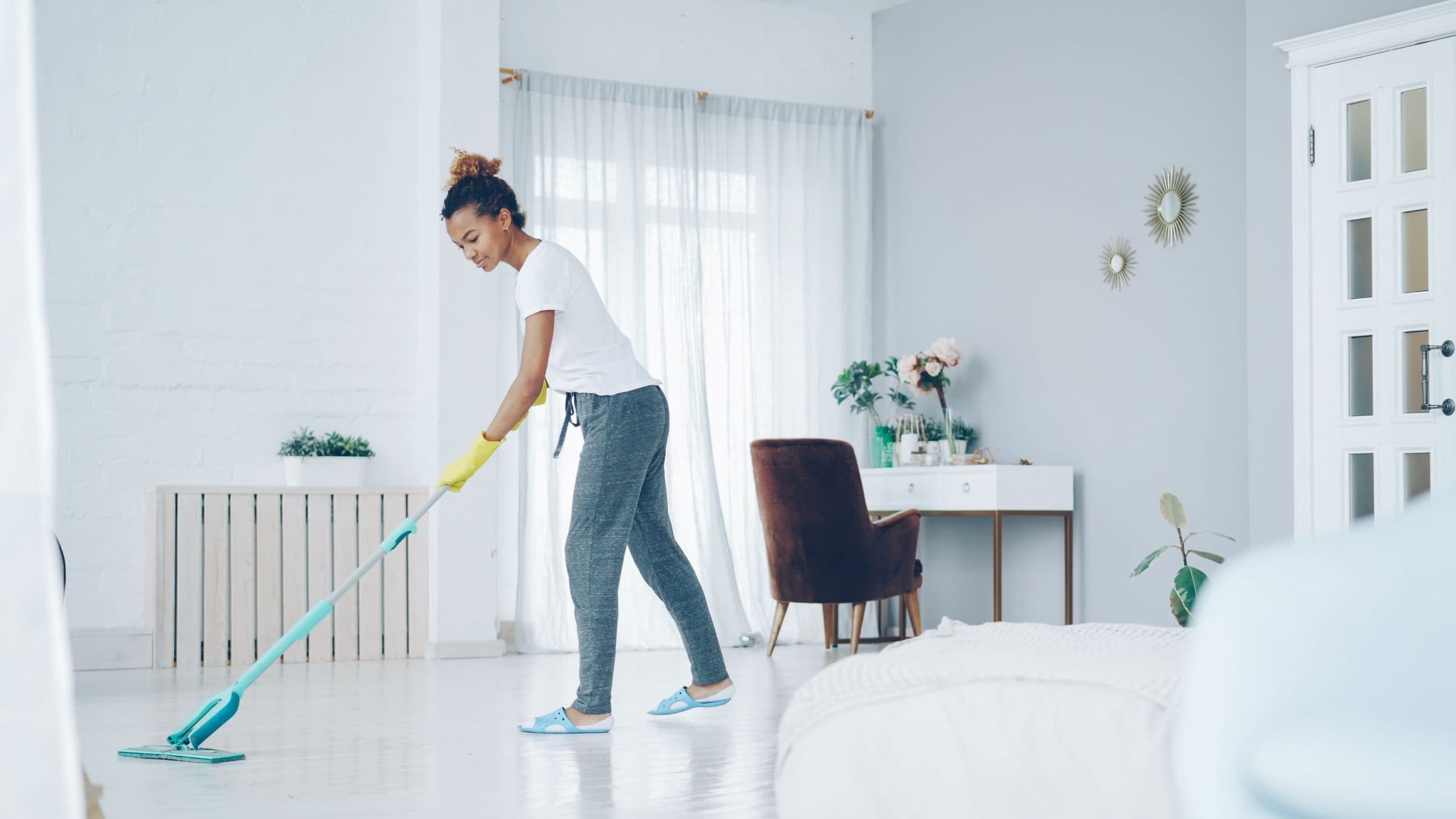 A cleaner mopping the hard floor of a bright, modern living room